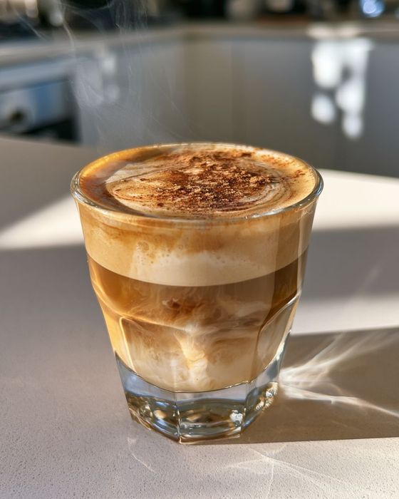Cinnamon honey cortado in a small glass on a wooden counter