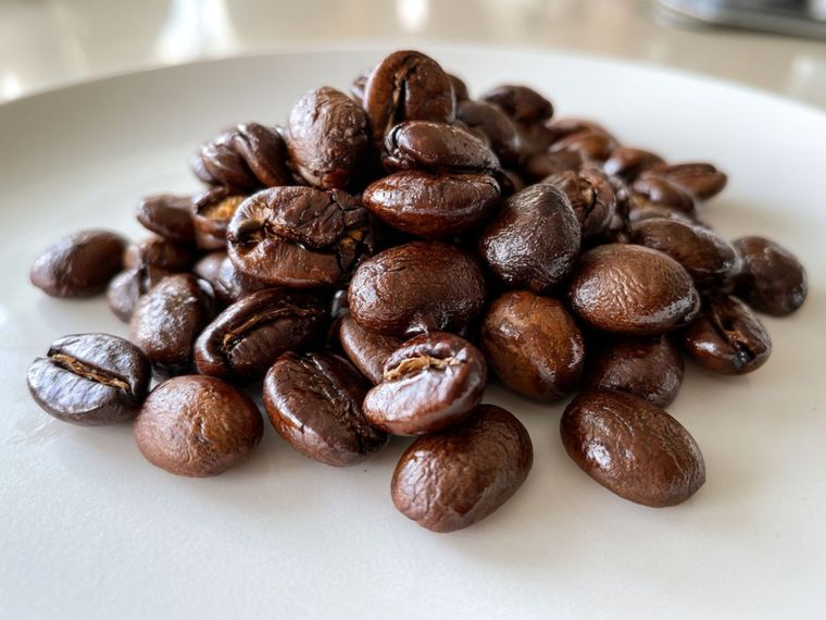 Dark roast coffee beans in a small white bowl